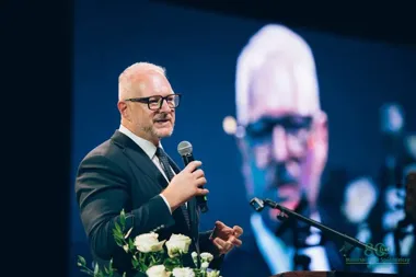 Mężczyzna w garniturze przemawia do mikrofonu podczas uroczystości jubileuszu 80-lecia Mazurskiego Banku Spółdzielczego w Ełku.